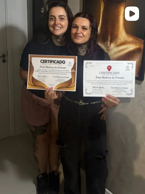 Nina Piercer ao lado de aluna recém-formada segurando o certificado do curso profissionalizante de Body Piercing